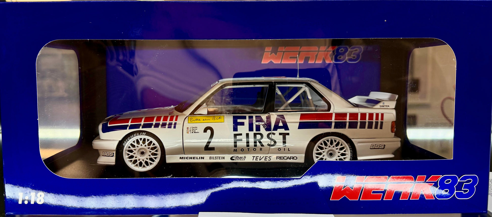 Model car in a blue display case with 'Fina First' branding.