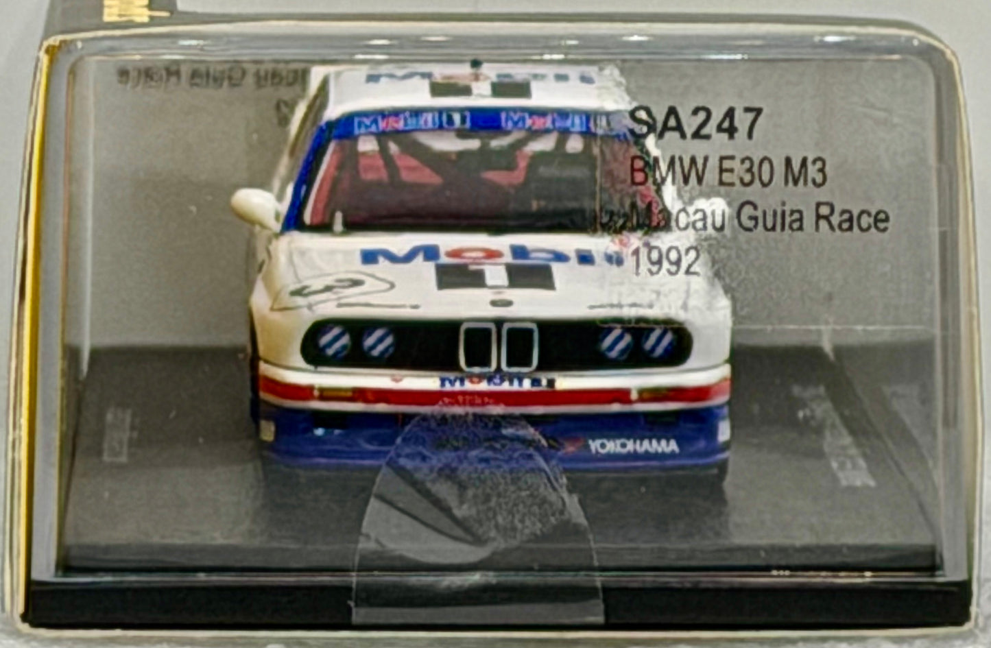 Model car of a BMW E30 M3 in a clear display case with branding and text.