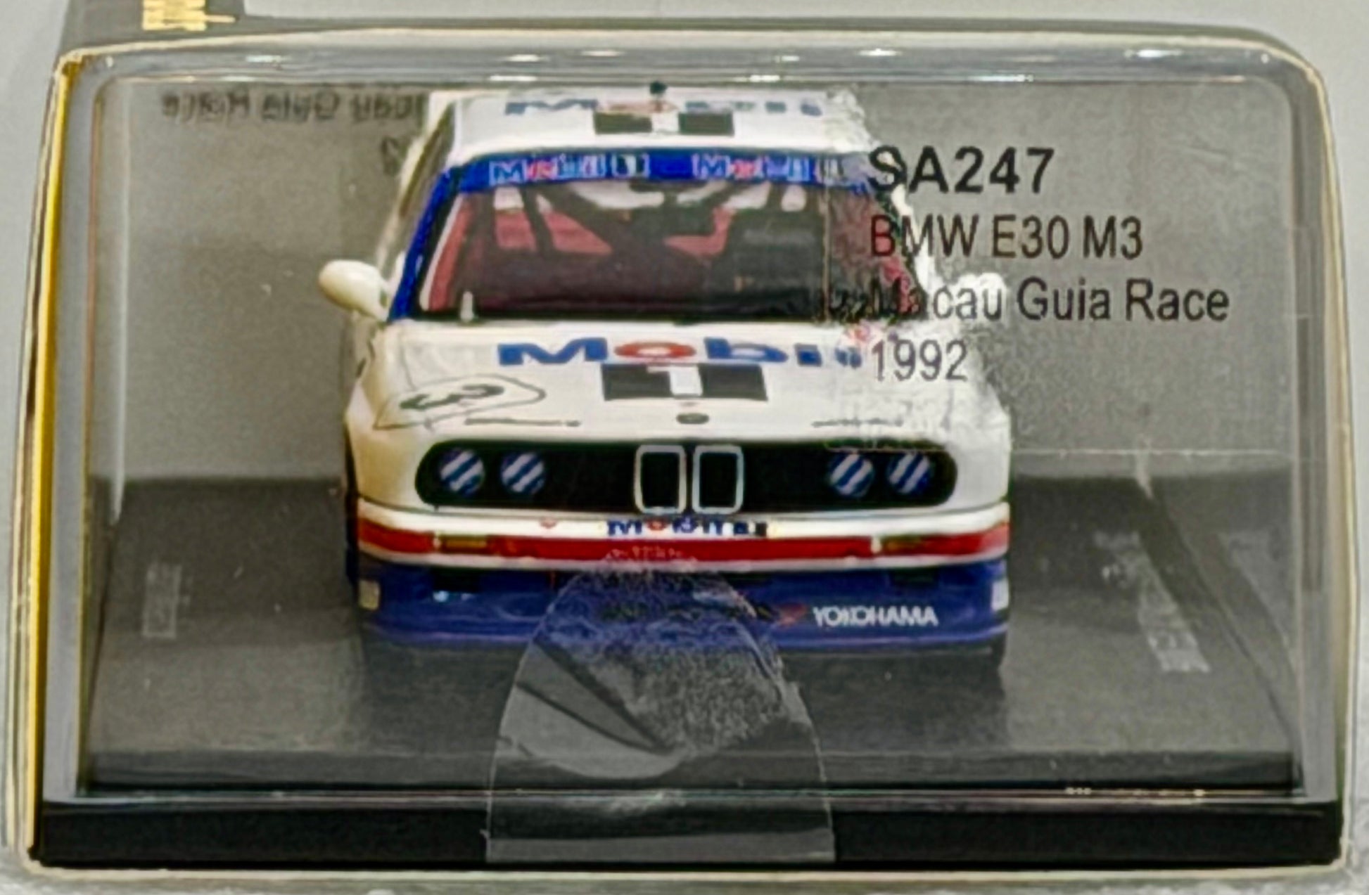 Model car of a BMW E30 M3 in a clear display case with branding and text.